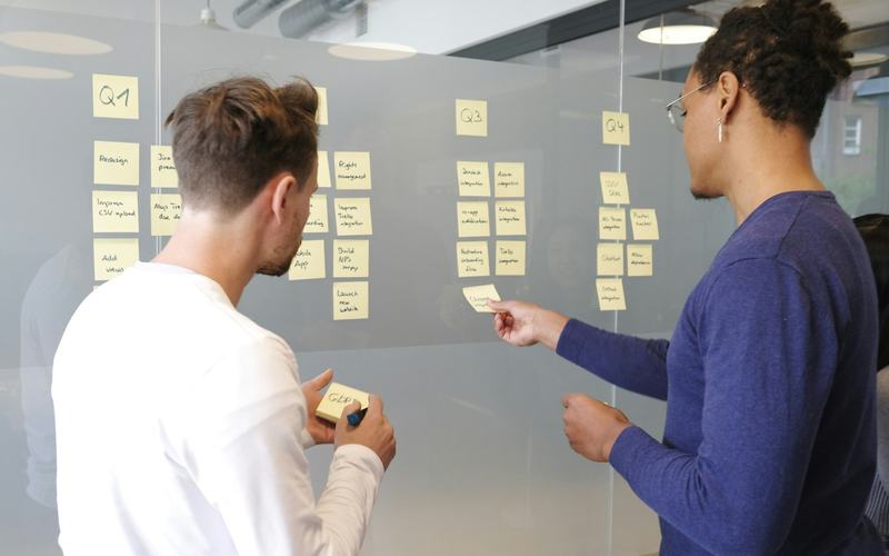 Two people planning work with sticky notes on a glass wall